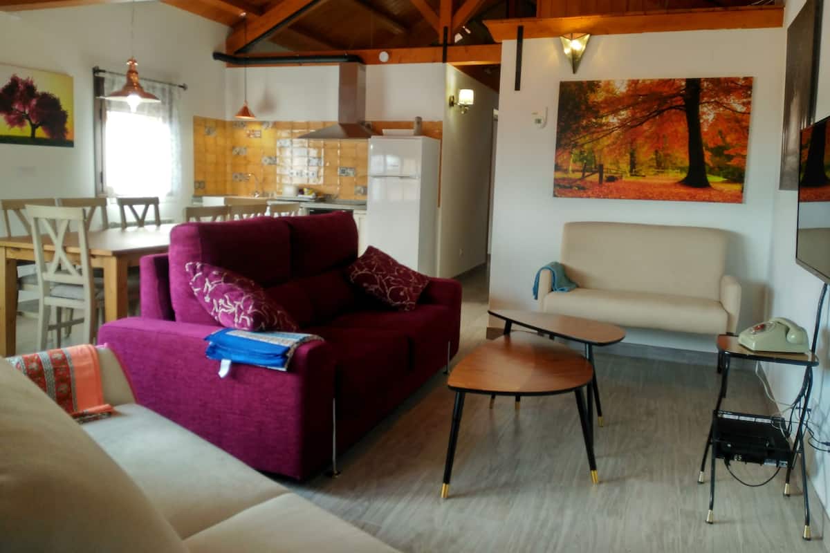 A living room with a red sofa, a beige sofa, a small table, and a kitchen in the background.