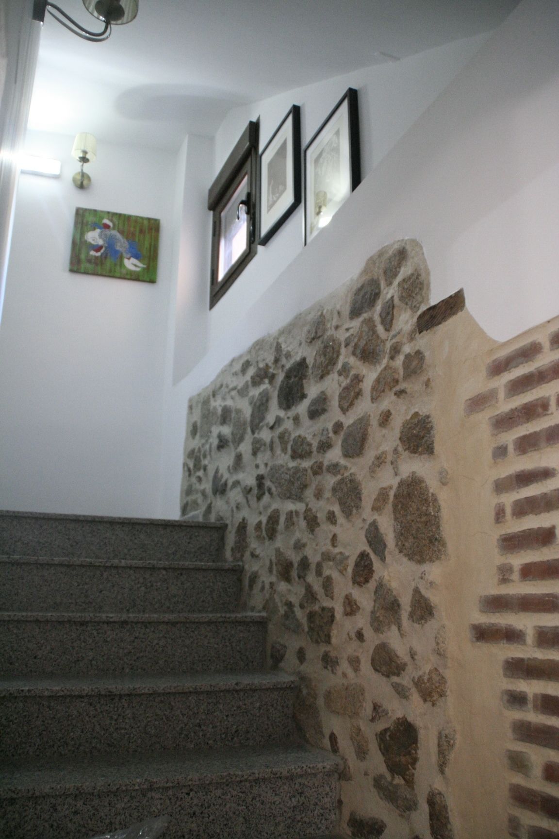 A staircase with stone walls and a brick section, leading to a landing with framed pictures.