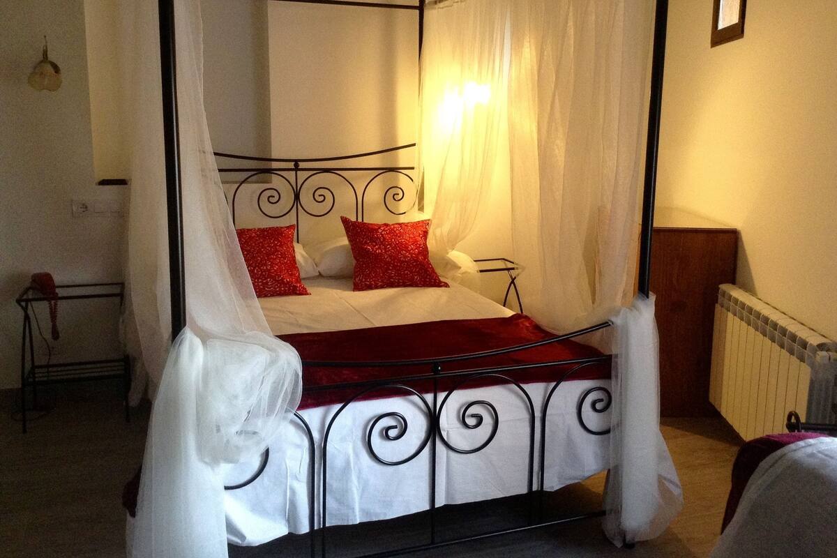 A four-poster bed with white and red bedding, a bedside table, and a radiator.