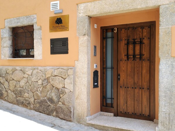 A rustic building with a stone wall, a wooden door with a number '3', and a signboard above the door.