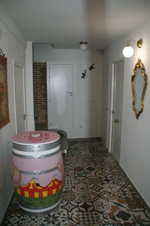 A hallway with patterned tiles, a large barrel, a mirror, and a door leading to a room.