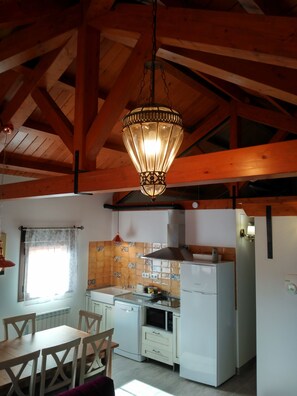 Une cuisine avec des poutres en bois, un luminaire suspendu, des appareils électroménagers blancs et un dosseret carrelé.