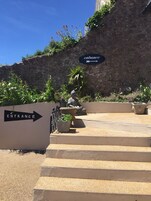 Un muro de piedra con un letrero que dice 'entrada', una estatua y escalones que conducen a un edificio.