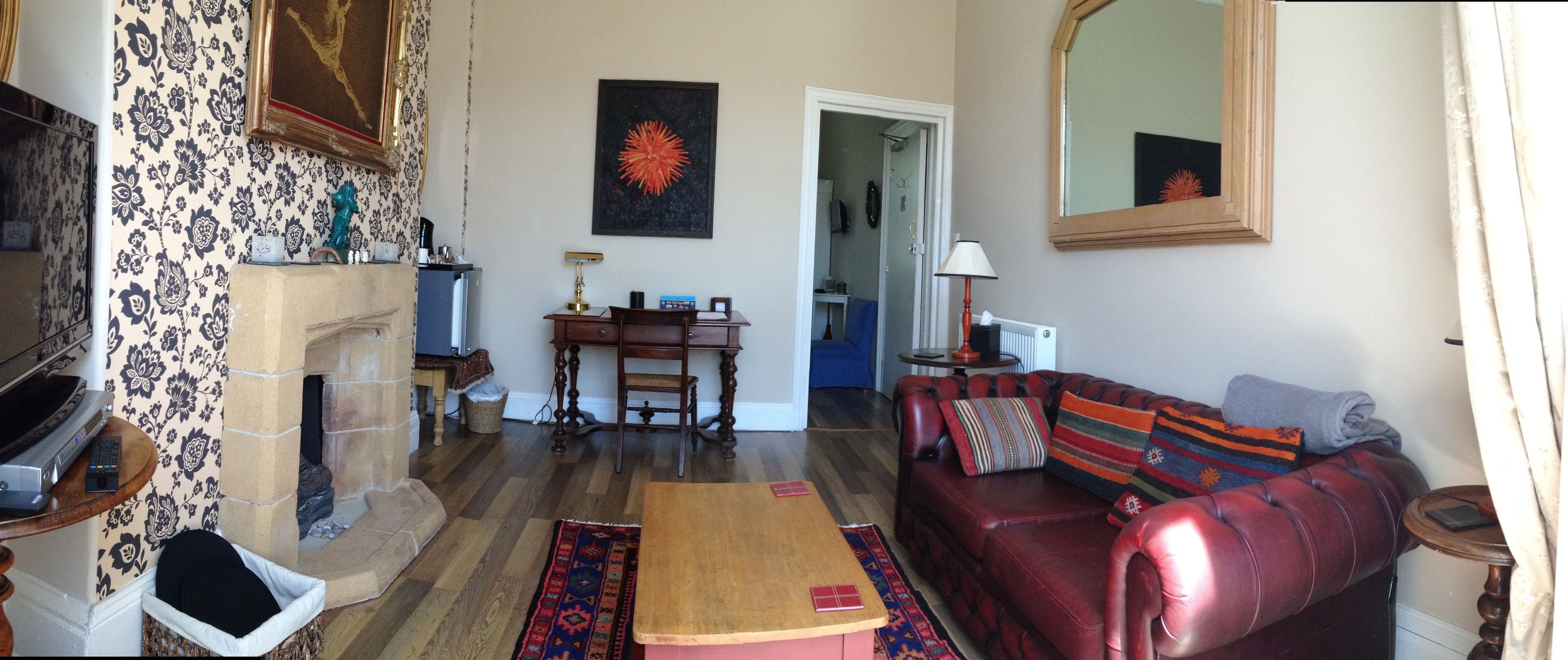 A living room with a fireplace, a red leather sofa, a wooden coffee table, and a patterned rug.