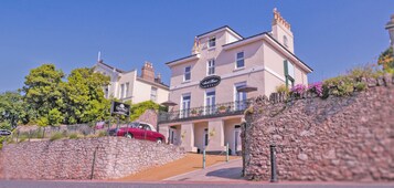 A hotel with a stone facade, a red car parked in front, and a clear blue sky.