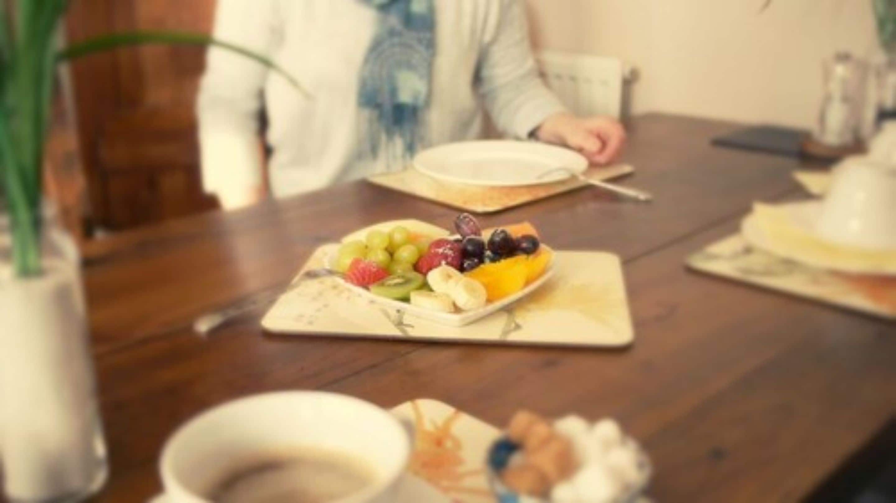 A dining table with a fruit platter, a cup, and a plate.