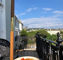 A balcony with a view of a cityscape, including buildings and greenery.