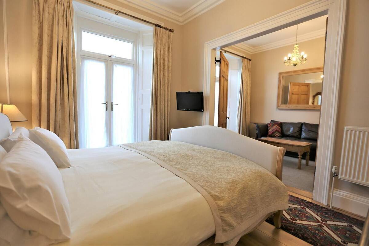 A hotel room with a large bed, a chair, a desk, a television, and a mirror.