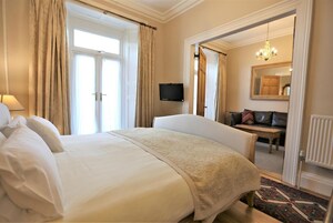 A hotel room with a large bed, a chair, a desk, a television, and a mirror.