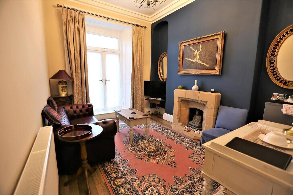 A living room with a sofa, armchair, fireplace, and a large mirror.