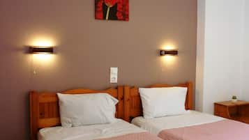 Una habitación de hotel con dos camas, cada una con cabecero de madera, ropa blanca de cama y cubrecamas acolchados color rosa. Hay lámparas de pared a cada lado de las camas, y un cuadro de una flor roja en la pared.