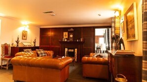 A cozy living room with a large sofa, a smaller armchair, and a fireplace. - The Bridge Guest House (Helmsdale)