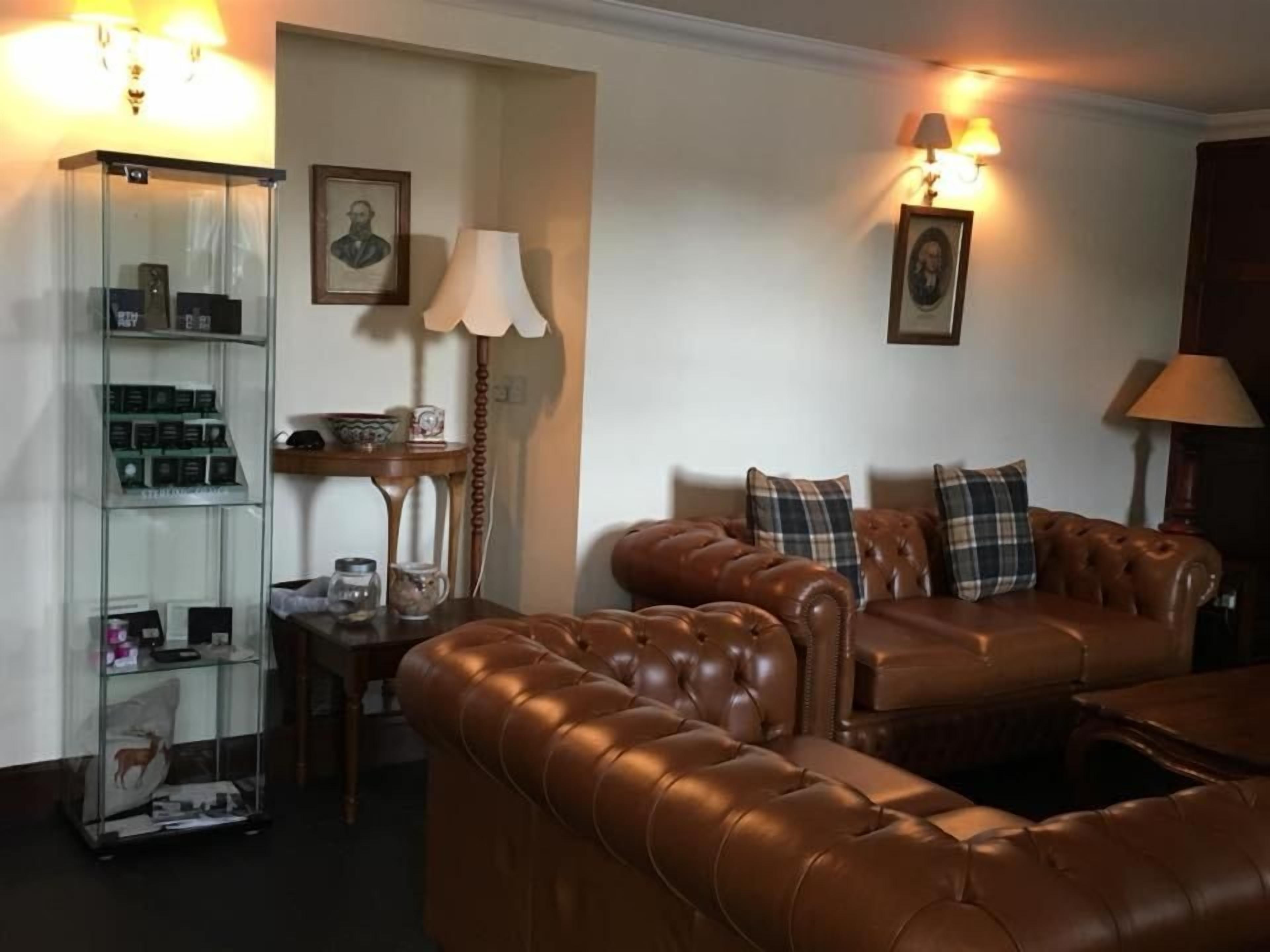 A living room with a brown leather sofa, a glass display cabinet, and a lamp.