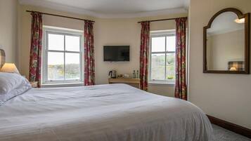 A hotel room with a large bed, a flat-screen TV, two windows with curtains, a bedside table, and a mirror.