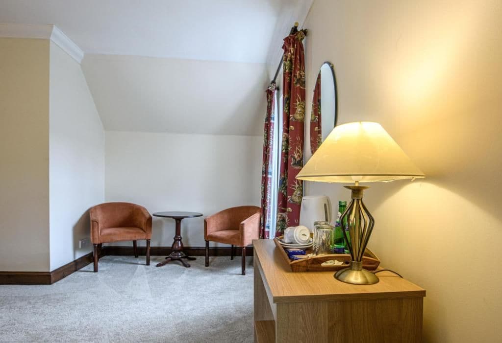 Une pièce comprenant deux fauteuils, une petite table ronde, une lampe et un miroir au mur.