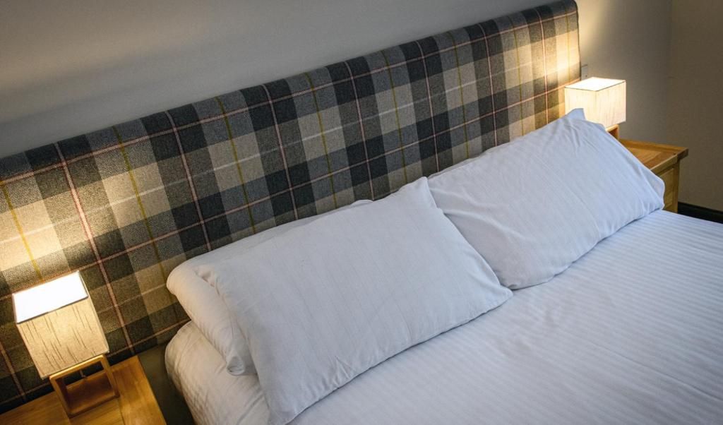 A bed with white linens, a plaid headboard, and two bedside lamps.