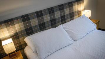 A bed with white linens, a plaid headboard, and two bedside lamps.