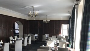 A dining area with multiple tables and chairs, a chandelier, and a view of the outdoors. - The Bridge Guest House (Helmsdale)