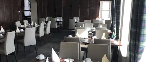 Een eetruimte met meerdere tafels en stoelen, een kroonluchter en uitzicht op het buitenland.