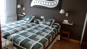 A double bed with a quilt, bedside tables, wall-mounted lamps, and a radiator. - Hostal Delgado (Benabarre)