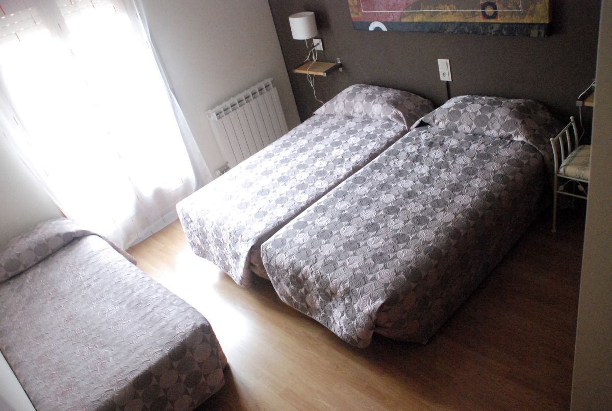 Een kamer met twee bedden, een stoel, een radiator, een lamp en een schilderij aan de muur.