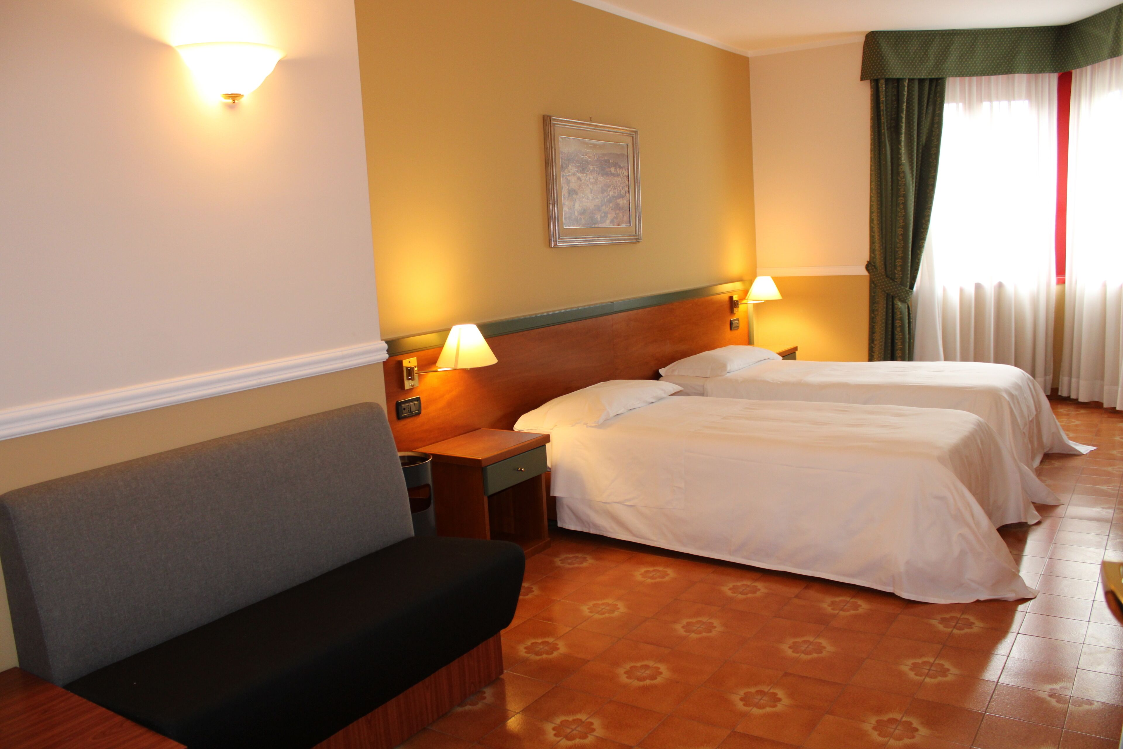 Habitación de hotel con dos camas, un sofá, una mesita de noche y una lámpara de pared.