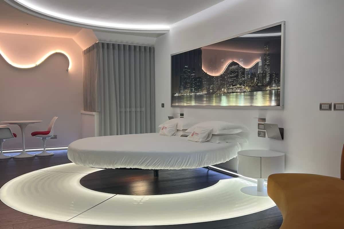A modern bedroom with a circular bed, a cityscape painting, and a unique ceiling design.