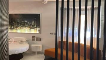 Una habitación de hotel moderna con una cama, una mesita de noche, un sofá y un cuadro de un paisaje urbano en la pared.