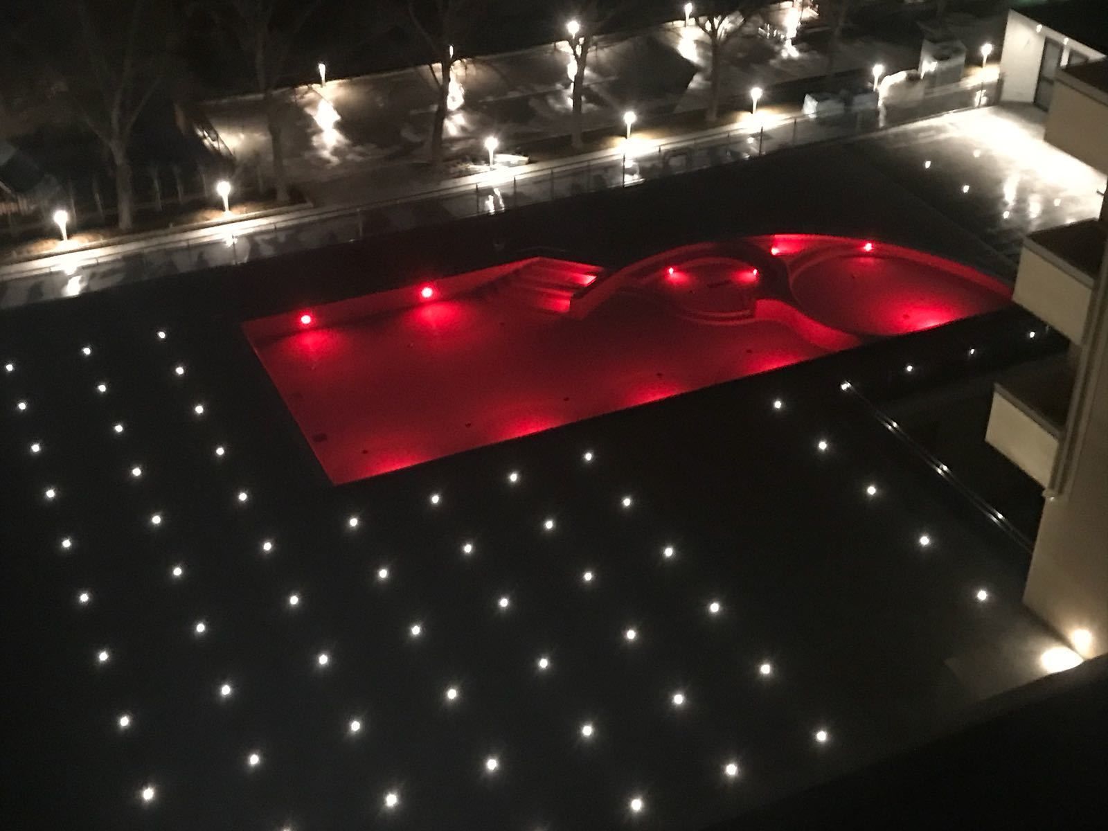 Una piscina en la azotea con iluminación roja y luces uniformemente distribuidas en el borde circundante.
