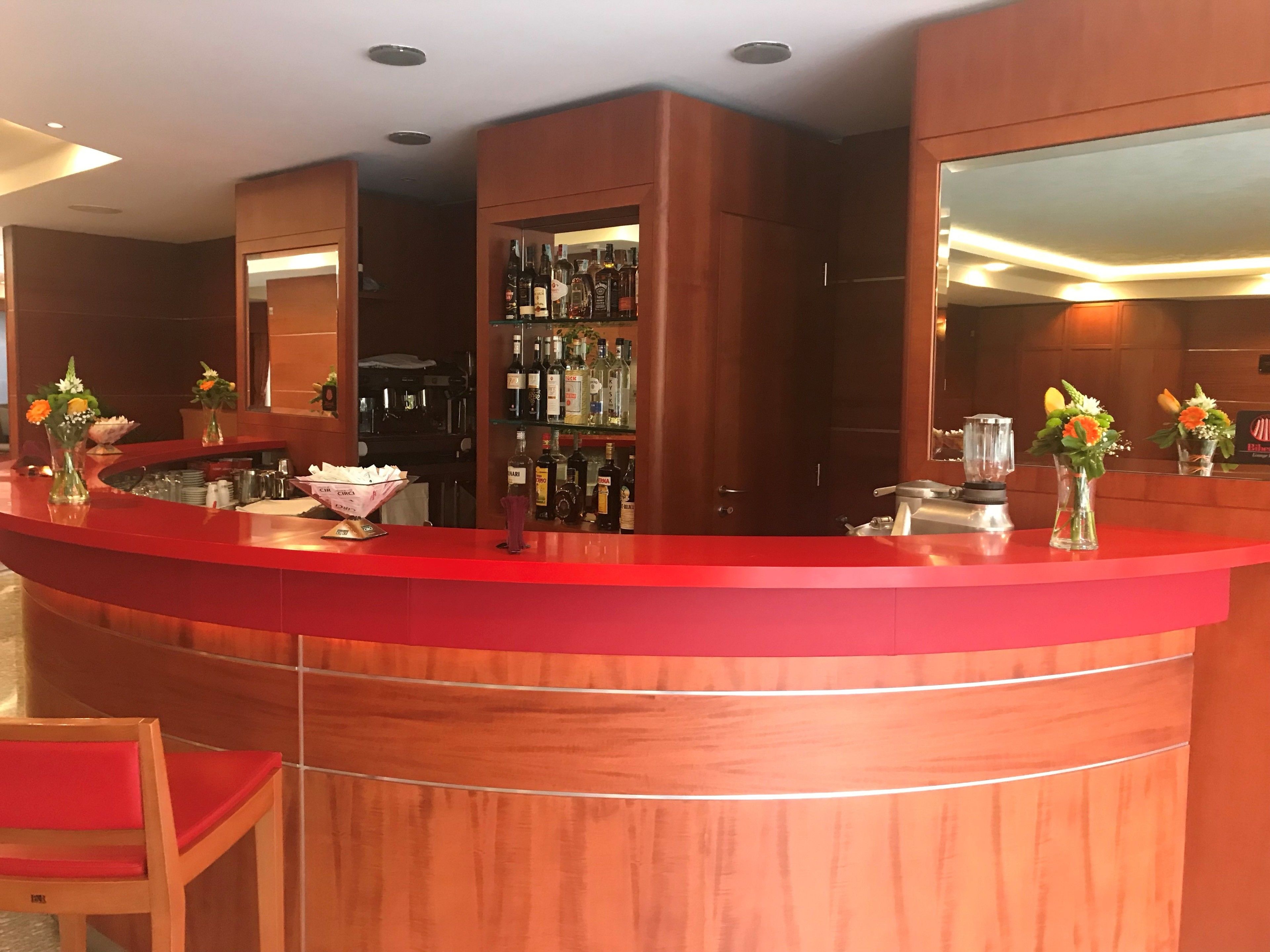 A hotel reception area with a red counter, a mirror, and a shelf with various bottles.