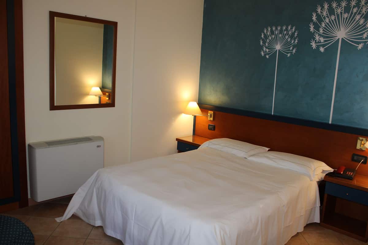 A hotel room with a bed, a nightstand, a lamp, a mirror, and a wall decoration.