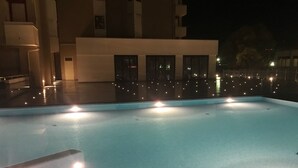 An outdoor swimming pool with steps leading into it, surrounded by a building with multiple windows and a fence. - Domus Grand Hotel (Rende)