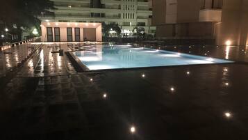 A nighttime swimming pool with a tiled deck and surrounding buildings.