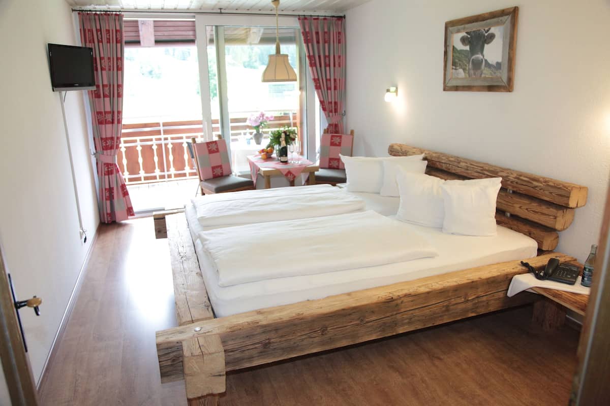 Un dormitorio con una cama de madera, una mesa con un florero y frutas, y vistas al exterior.