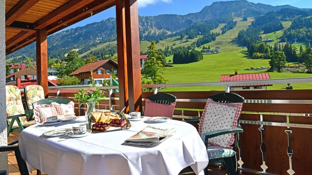 A covered outdoor dining area with a table set for two, overlooking a mountainous landscape. - Hotel Zum Senn (Bad Hindelang)