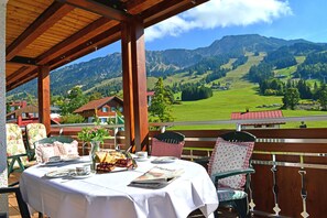 A covered outdoor dining area with a table set for two, overlooking a mountainous landscape. - Hotel Zum Senn (Bad Hindelang)