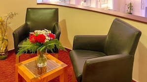 Una habitación con techo curvo, ventanas arqueadas, un sillón de cuero verde, una mesa de madera con un florero y una alfombra roja.
