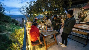 Un espace de restauration en plein air, avec des tables et des bancs, entouré de verdure et offrant une vue sur des collines lointaines.