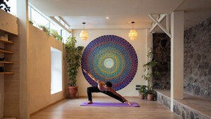 A yoga room with a large circular wall tapestry, wooden floors, and potted plants. - Supertramp Hostel Cusco (Cusco)