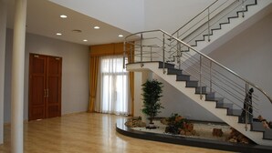 A spacious room with a curved staircase, a wooden door, and a large window with curtains. - Lo Raco de l’Olivera (Granyanella)