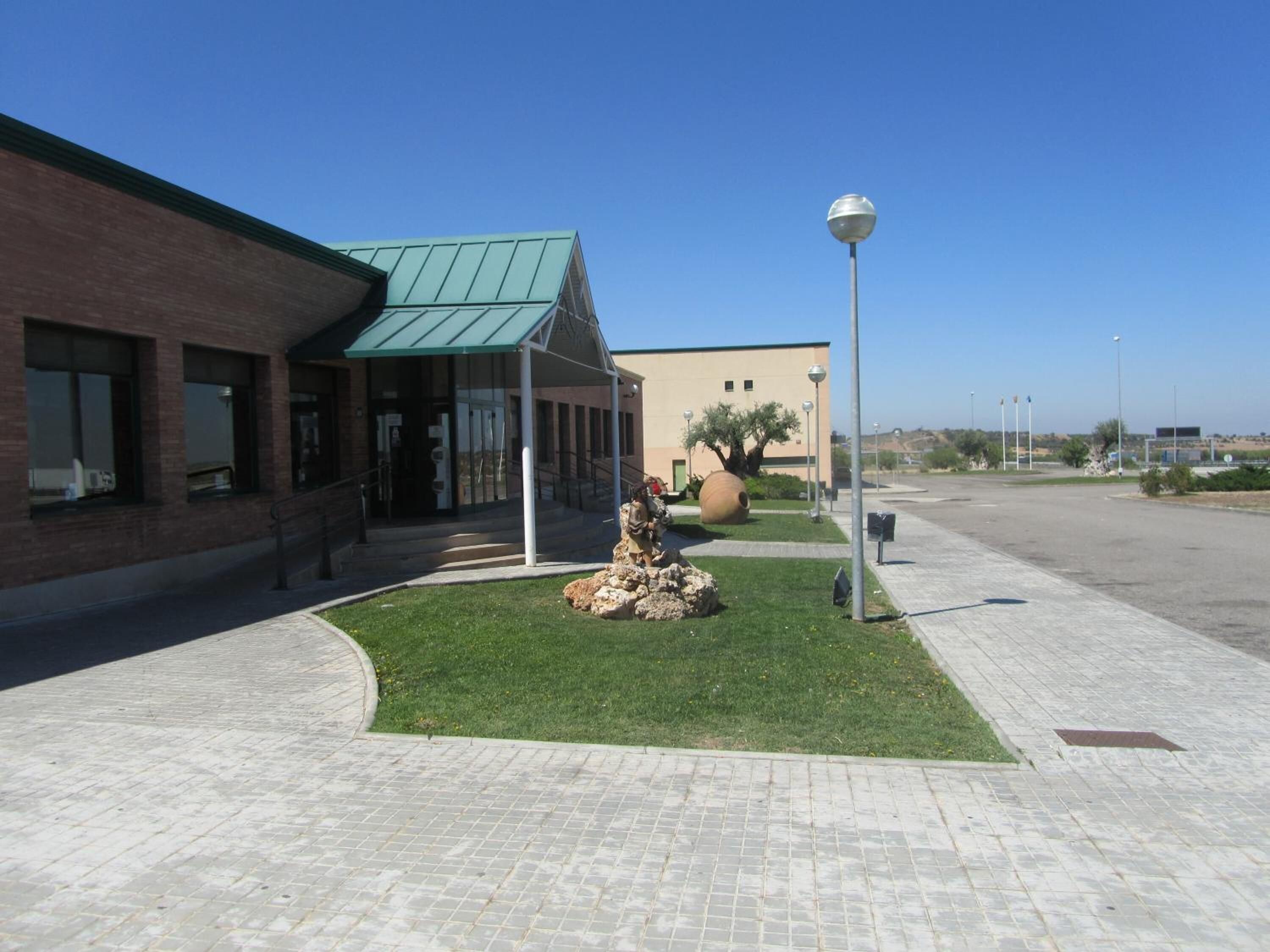 A building with a green roof, a paved walkway, and a landscaped area with rocks and a tree.
