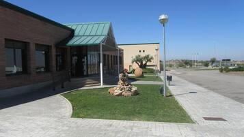 A building with a green roof, a paved walkway, and a landscaped area with rocks and a tree.