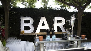 A bar area with a sign that reads "BAR" in large letters. There are glasses and bottles on the counter, and a small fruit display. - Lo Raco de l’Olivera (Granyanella)