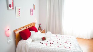 A neatly made bed with white bedding and red pillows, a bedside table with a lamp, and a bouquet of flowers on the bed.