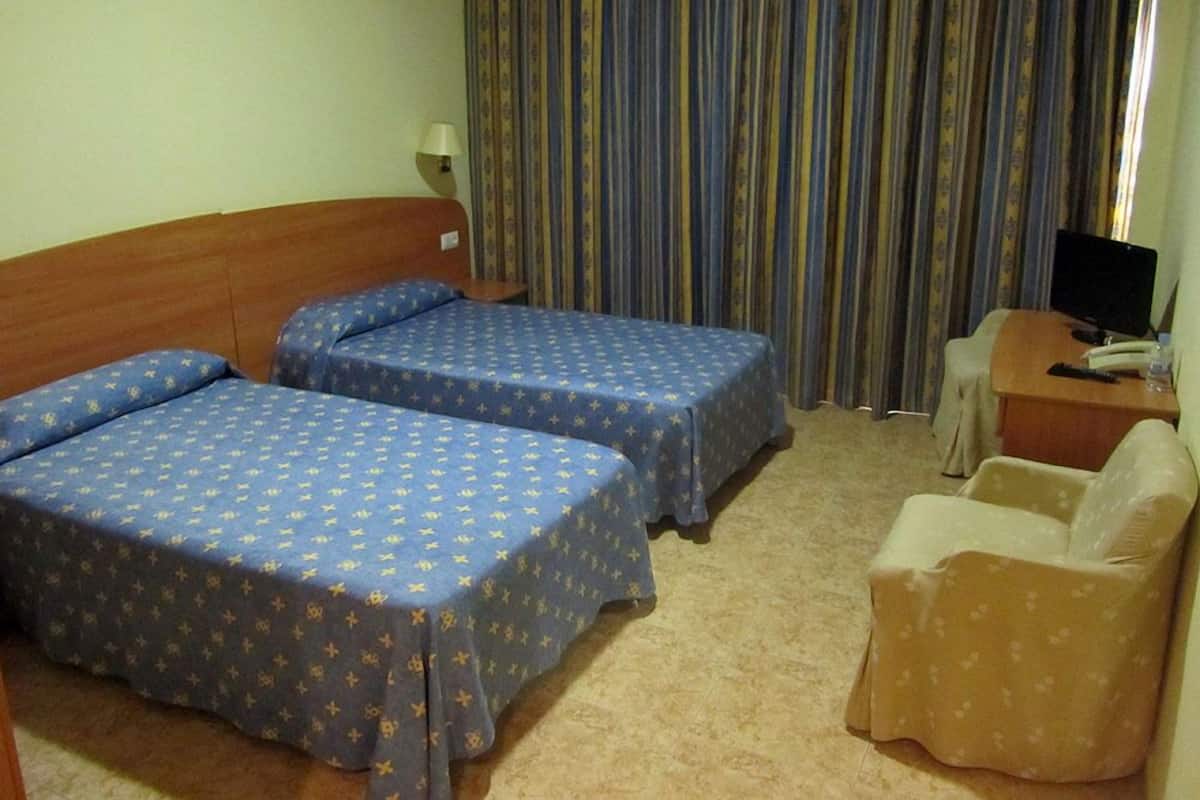A hotel room with two beds, a desk with a computer, and a chair.