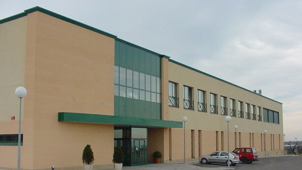 A modern building with a flat roof, large windows, and a green awning. There are two cars parked in front.