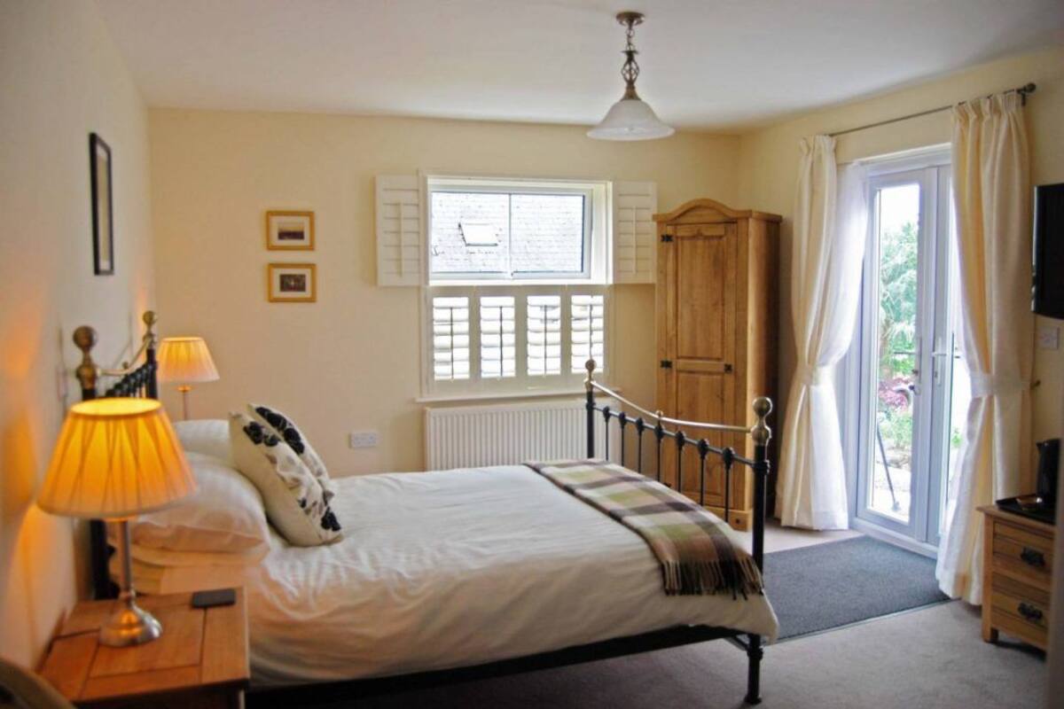 A bedroom with a bed, bedside lamps, a window with shutters, a wooden wardrobe, and a television.