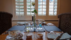 A dining table set with fine china, glassware, and a vase with a single flower. - Highbury Garden Suite (Boncath)