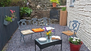 A garden with a stone wall, a wooden fence, and a metal bench with cushions. - Highbury Garden Suite (Boncath)