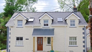 A two-story house with a gabled roof, a front porch, and a small garden area. - Highbury Garden Suite (Boncath)